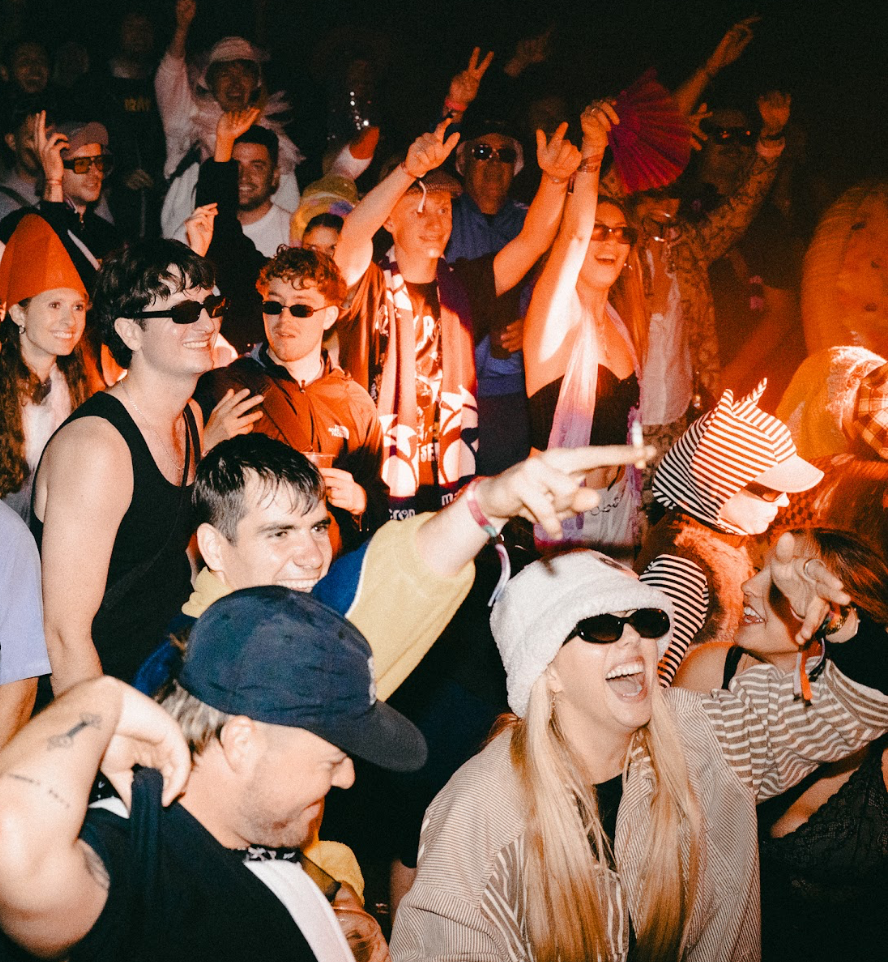 Energetic festival crowd at night with warm orange lighting and someone holding a colorful hand fan