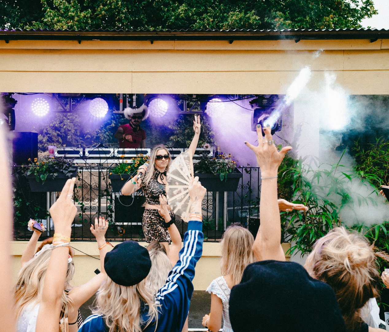 Performer on stage with hand fan singing to crowd at daytime festival